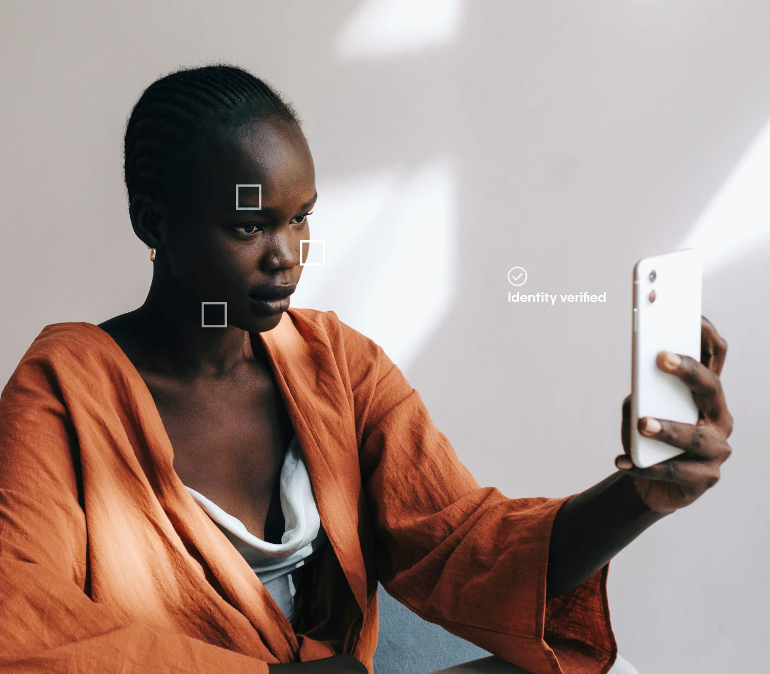 A person in an orange robe uses a smartphone for facial recognition; square markers highlight facial features, and “identity verified” appears on the image.